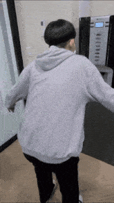 a person wearing a grey hoodie is standing in front of a vending machine .