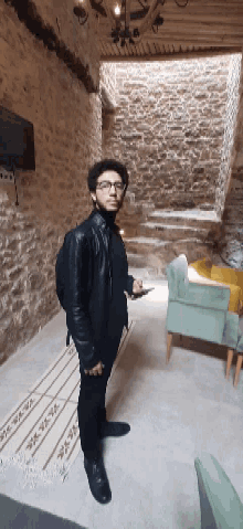 a man in a leather jacket and glasses stands in a room