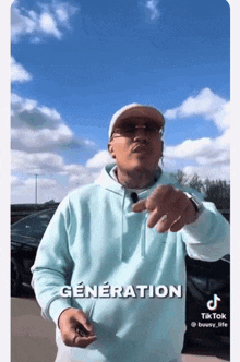 a man wearing a light blue hoodie and a hat is pointing at the camera with generation written on the bottom