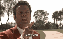 a man in a red suit and white shirt is pointing at the camera and saying " i hate you "