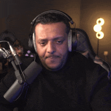 a man wearing headphones sits in front of a microphone with a lamp in the background