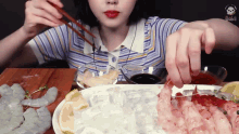 a woman is eating shrimp with chopsticks and a bowl of sauce