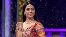 a woman in a colorful dress is standing on a stage and looking at the camera .