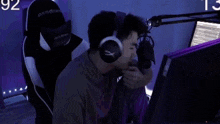 a man wearing headphones and a gaming chair is sitting in front of a computer screen .