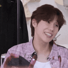a young man wearing a plaid shirt and a white tank top is smiling