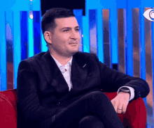 a man in a suit is sitting in a red chair with his legs crossed