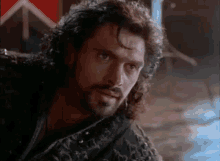 a man with a beard and long curly hair is looking at the camera .