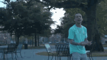 a man in a green shirt is standing in a park giving the middle finger .