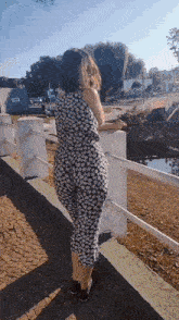 a woman in a black and white floral dress leans on a railing looking out over a body of water