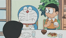 a cartoon character named doraemon is sitting at a table with a boy eating food .