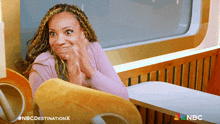 a woman sitting at a table with a nbc logo on the bottom left