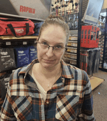 a woman wearing glasses and a plaid shirt is standing in front of a display of rapala gear bags