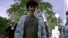a young boy with curly hair is wearing a blue jacket and smiling while standing in a park .