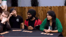 a group of people are sitting at a table playing a game of cards .