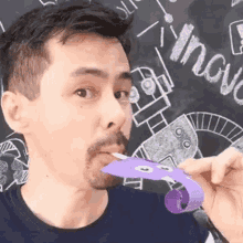 a man with a beard is holding a purple object in his mouth in front of a blackboard that says innovation