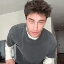 a young man wearing a gray t-shirt and a white turtleneck is standing in a room .