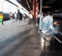 a man sits on a bench at a train station and looks at his cellphone