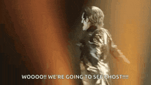 a man in a gold jacket is dancing on a stage and saying `` we 're going to see ghost ! ''
