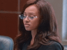 a woman wearing glasses and a black shirt is sitting in a chair in a room .