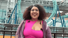 a woman in a pink top is smiling in front of a rollercoaster