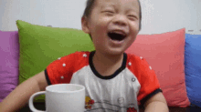 a little boy is laughing while holding a cup