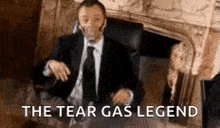 a man in a suit and tie is sitting in front of a fireplace .