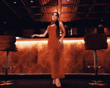 a woman in a red dress stands in front of a bar in a dark room