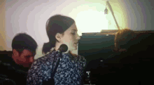 a woman singing into a microphone with a man behind her playing a piano