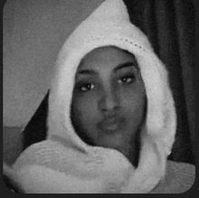 a black and white photo of a woman wearing a knitted hooded scarf .