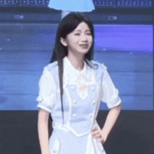 a woman in a blue and white dress is standing with her hands on her hips and smiling .