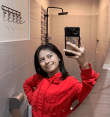 a woman in a red hoodie is taking a selfie with her phone