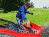a man in a blue shirt is standing next to a red car with the words yeet yeet written on it