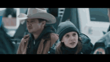 a man in a cowboy hat stands next to a woman in a black hat