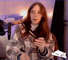 a woman wearing a plaid shirt is sitting in front of a microphone with a sticker of a cat behind her