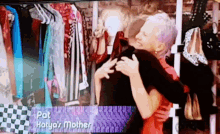 a woman is hugging another woman in front of a display of clothes and the name pat that is on the screen