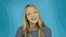 a woman in a grey shirt is making a funny face against a blue background