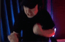 a man in a black shirt is making a fist gesture in front of a red curtain .