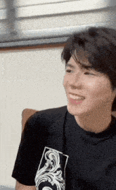 a young man wearing a black t-shirt with a white design on it smiles