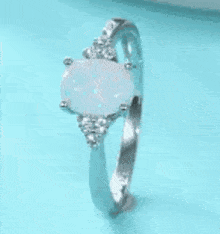 a silver ring with a white opal and diamonds is on a blue surface .