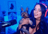 a woman wearing headphones holds a small dog in front of a shure microphone