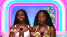 a couple of women sitting next to each other holding glasses of wine