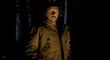 a man in a jacket is standing in a dark forest with trees in the background .