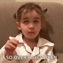 a little girl in a halloween costume is sitting on a couch eating candy and making a funny face .