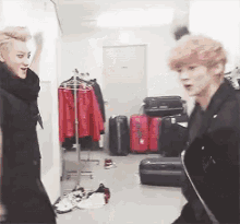 two men are standing in a room with luggage and clothes hanging on racks
