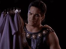 a man in a leather vest is holding a purple cloth and a crown .