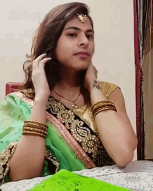 a woman wearing a green and gold saree is sitting at a table