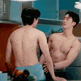 two shirtless men are standing next to each other in a kitchen and talking to each other .