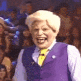 a man wearing a purple vest and a yellow tie is smiling in front of a crowd