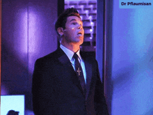 a man in a suit and tie with a cross around his neck is standing in front of a sign that says dr pflaumisen