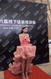 a woman in a pink dress is standing on a red carpet and holding a microphone